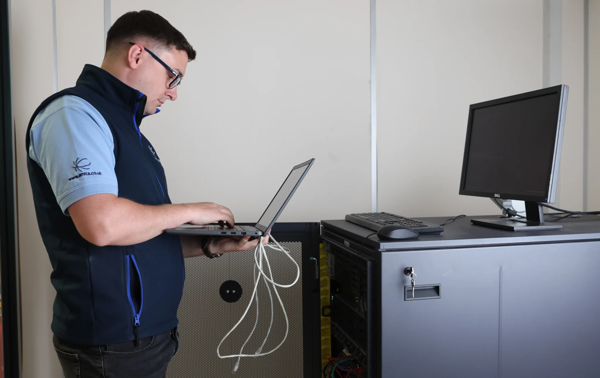 a man working on his laptop beside a server rack